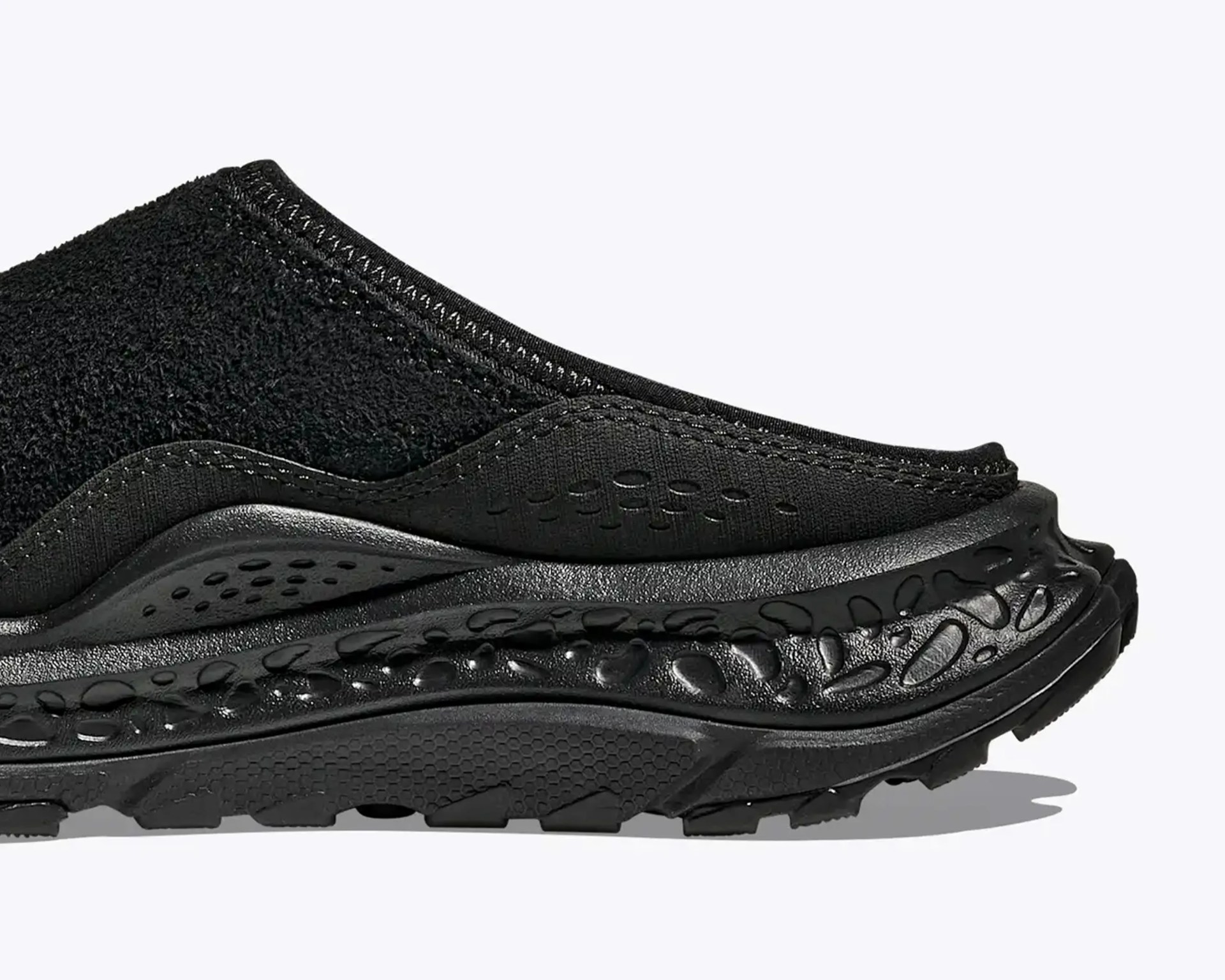 Close-up of the black sneaker's midsole and heel area featuring textured and perforated design elements.