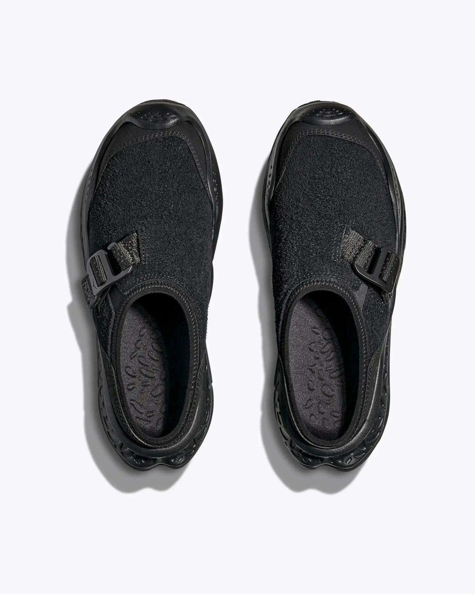 Pair of black slip-on shoes with textured fabric uppers and adjustable side buckles, viewed from above.