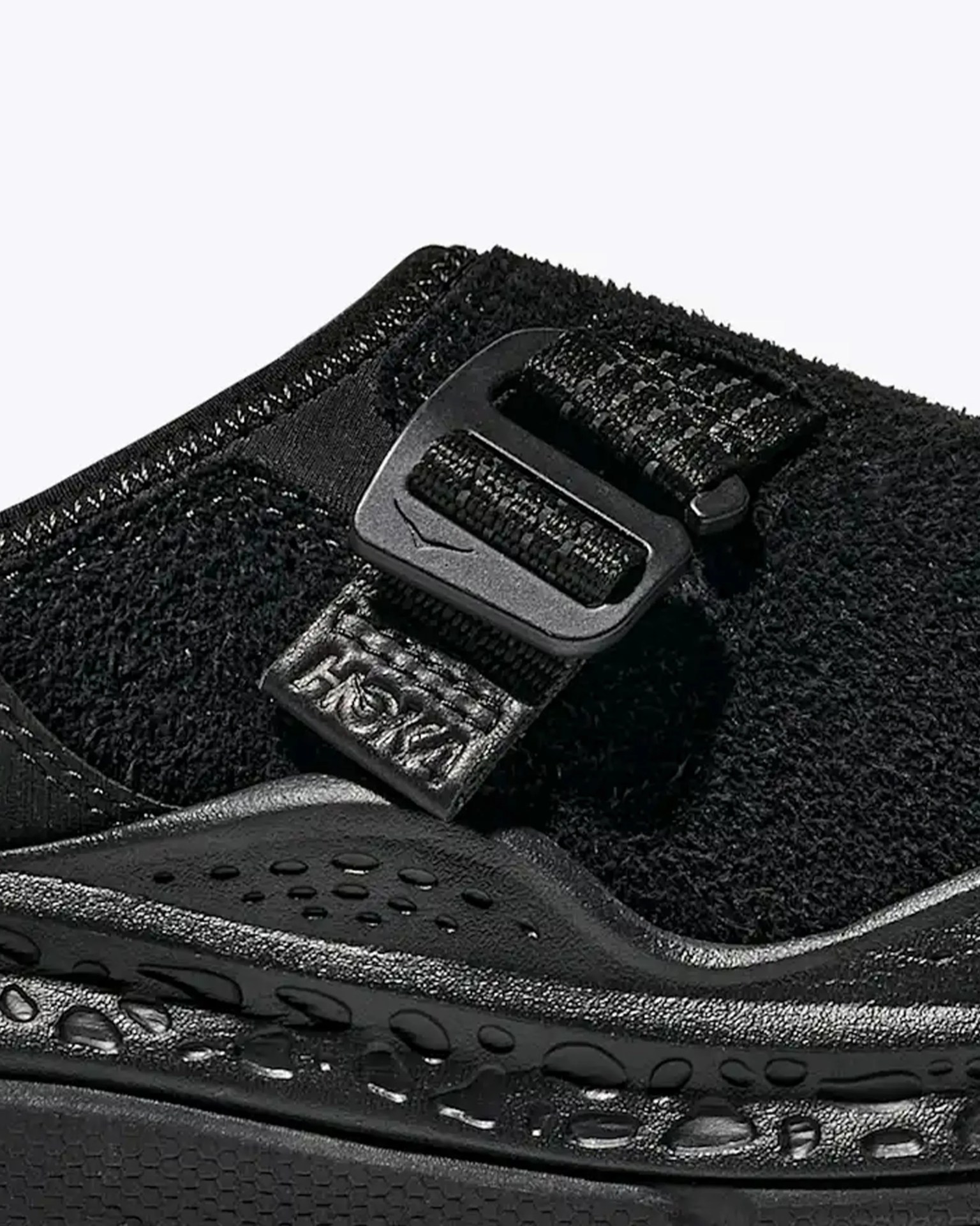 Close-up of black Hoka shoe strap with plastic buckle and textured midsole.