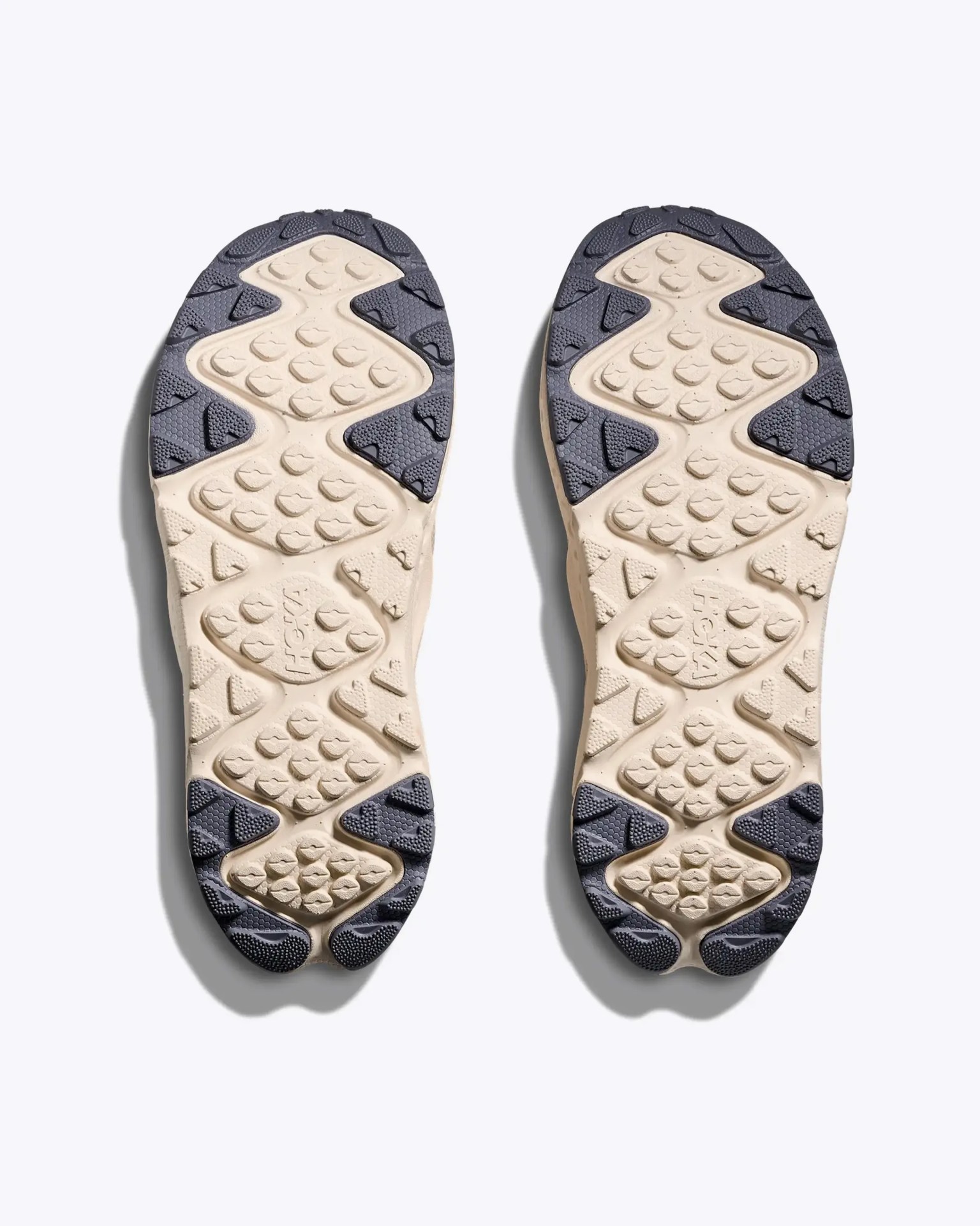 Beige and black rubber shoe soles with textured grip pattern and "HOKA" branding in the center.