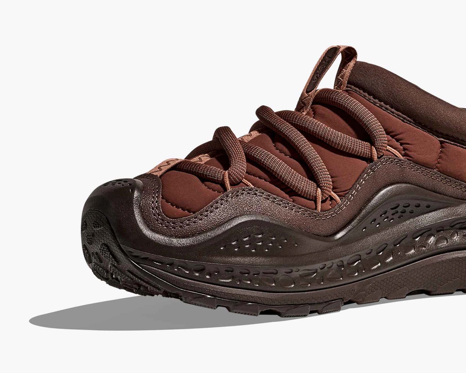 Brown sneaker with thick textured sole and padded upper with loop pull tab.