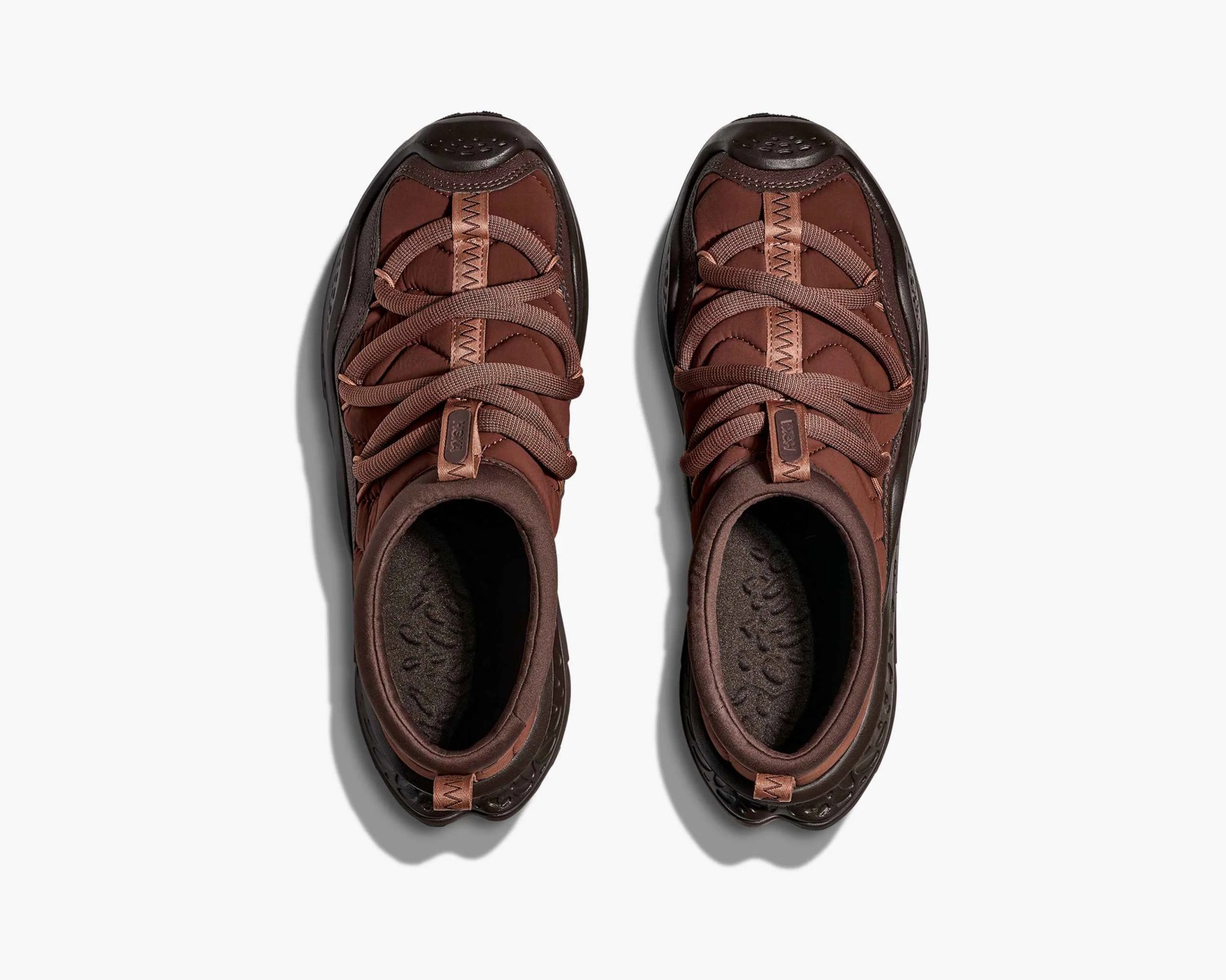 Pair of brown athletic shoes with thick laces viewed from above on a white background.