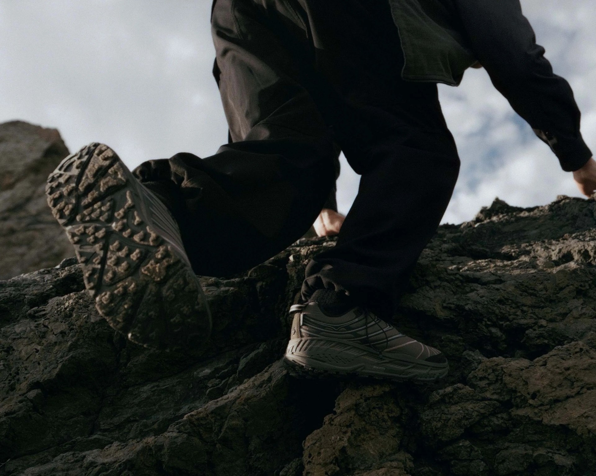 Person wearing black pants and gray hiking shoes climbing rocky terrain.