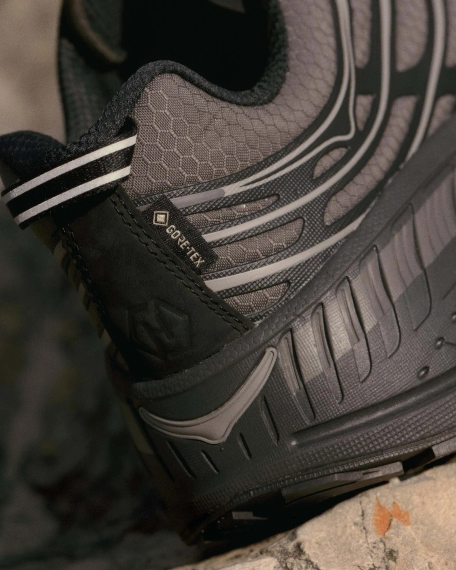 Close-up of a gray and black Gore-Tex hiking shoe with textured fabric and rubber sole on a rock.