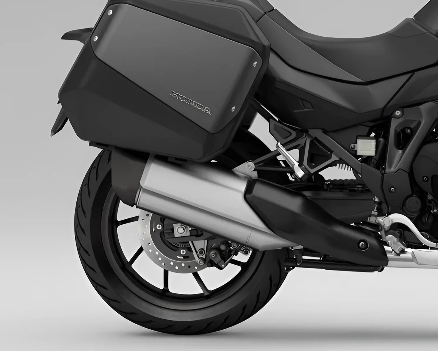 Rear wheel and exhaust of a black motorcycle with a hard side pannier labeled "Honda.