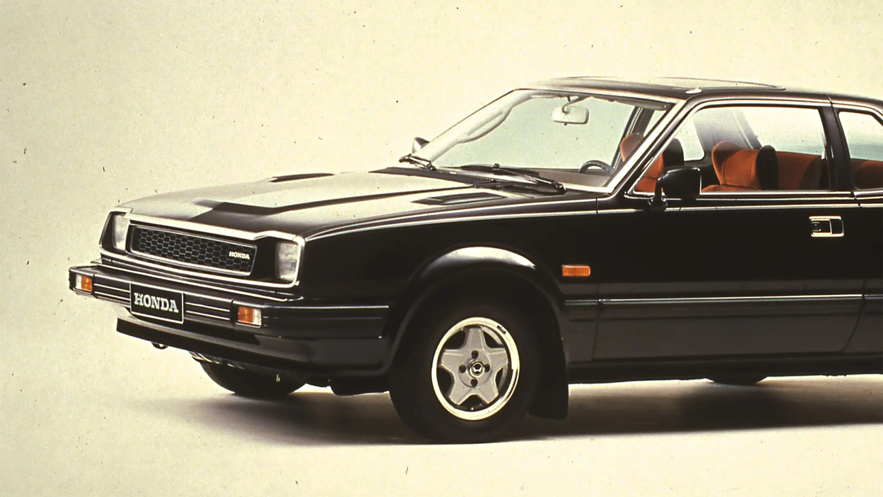 Black vintage Honda sedan with orange interior seats and silver five-spoke wheels.