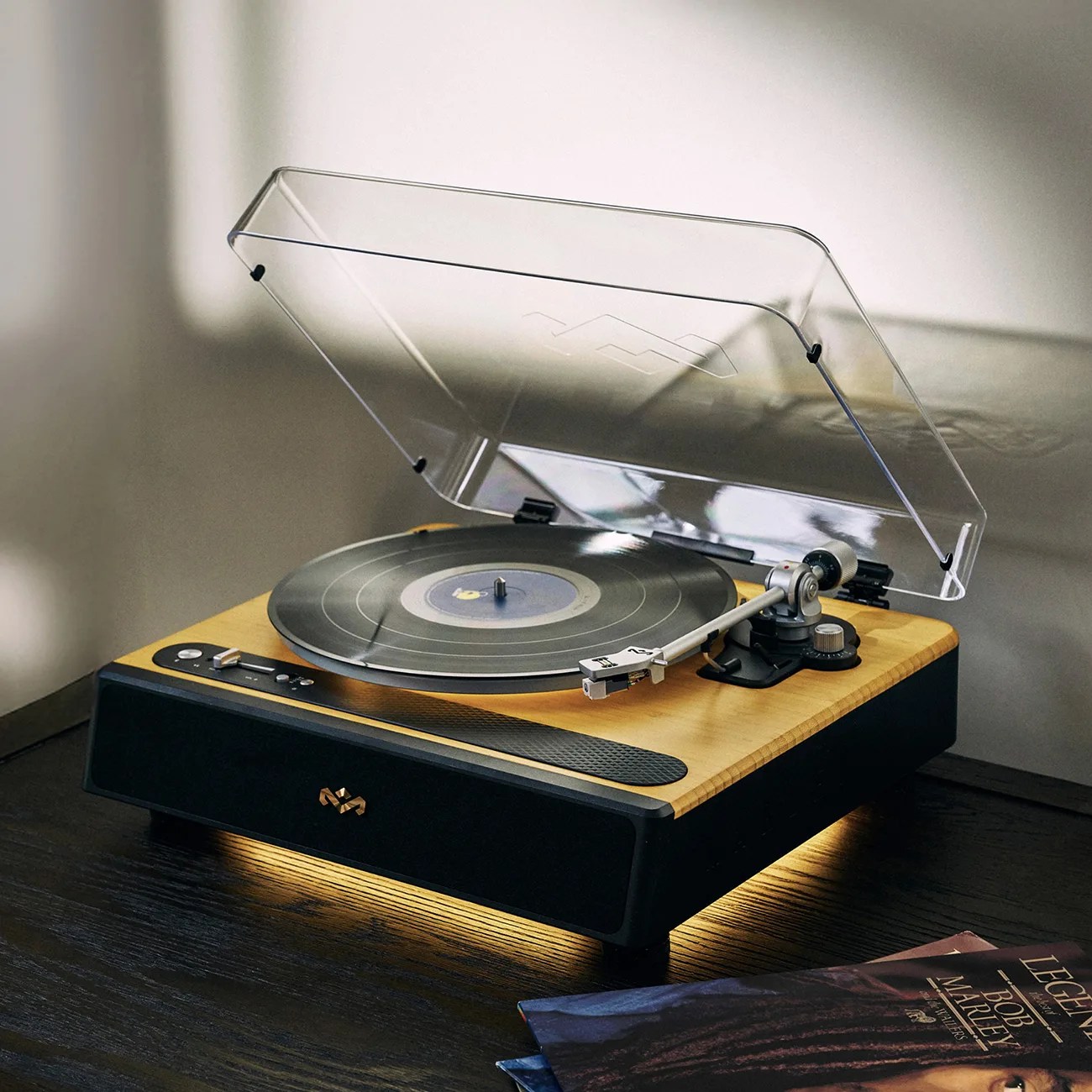 Wood and black turntable with clear dust cover open, playing a vinyl record on a dark wooden surface.