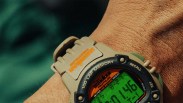 Digital sports watch with beige strap and green backlit display worn on a wrist.