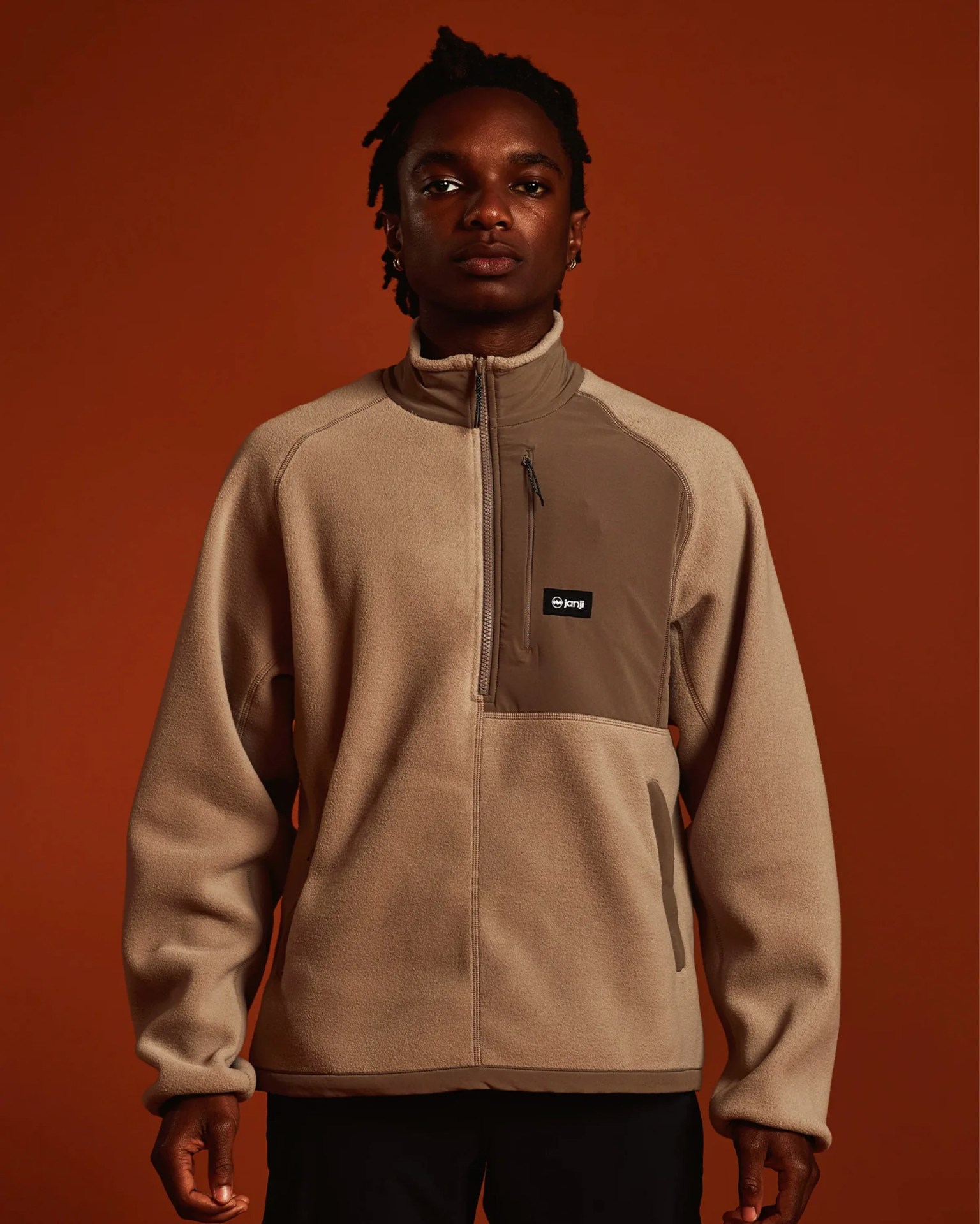 Beige and brown quarter-zip fleece pullover with chest pocket and Janji logo worn by a person.