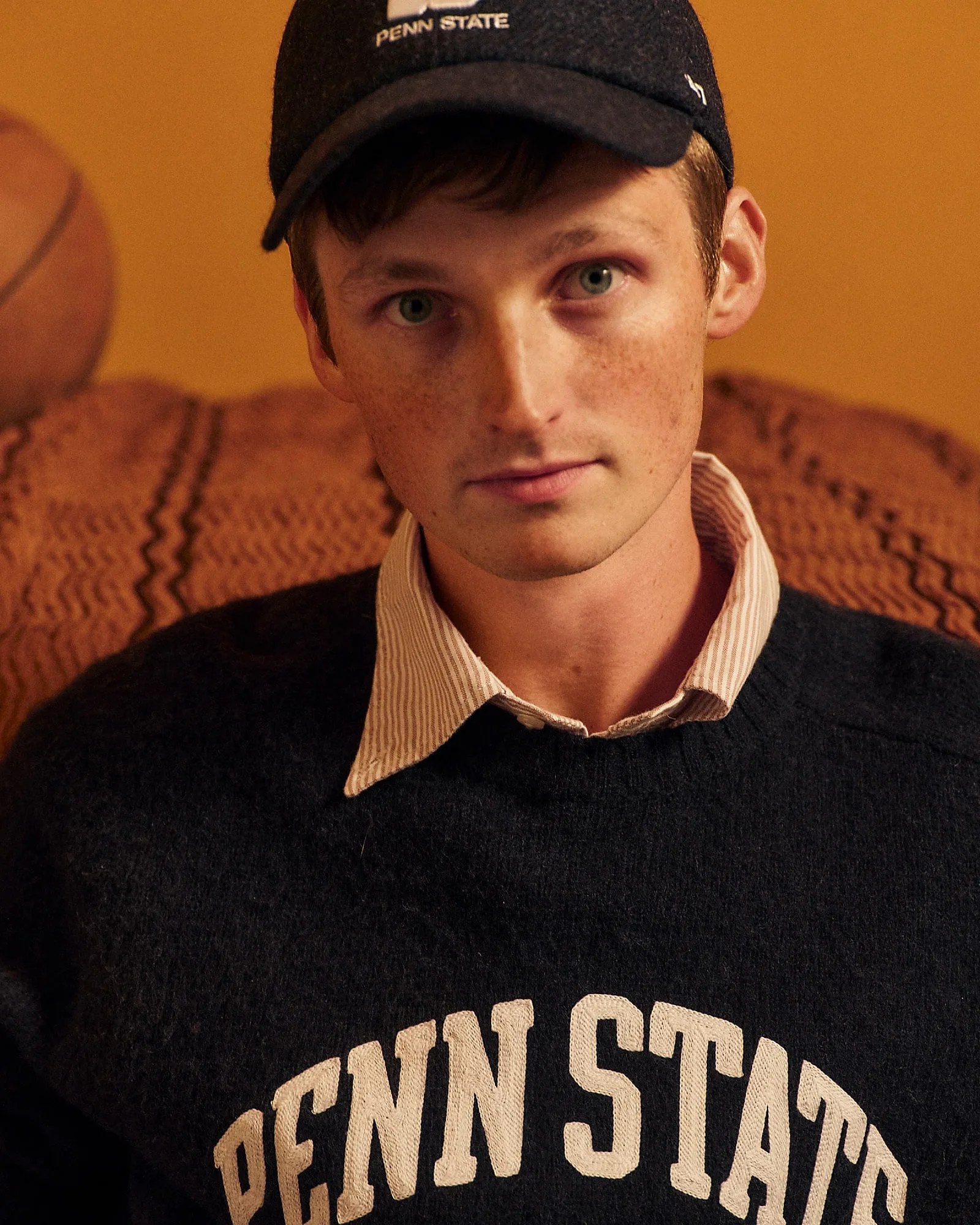 Young man wearing a black Penn State cap and a black sweater with "PENN STATE" text over a striped collared shirt.