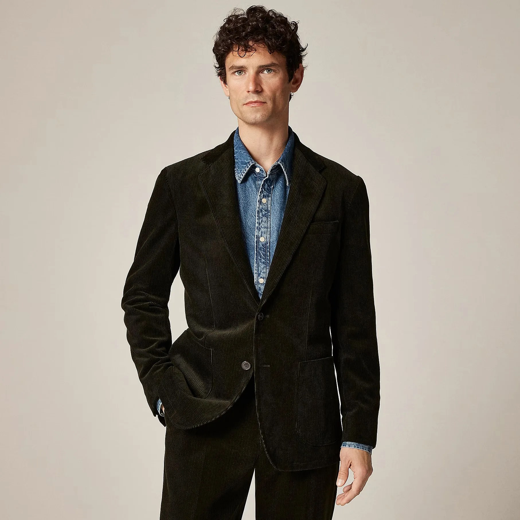 Man wearing a dark brown corduroy blazer over a blue denim button-up shirt.