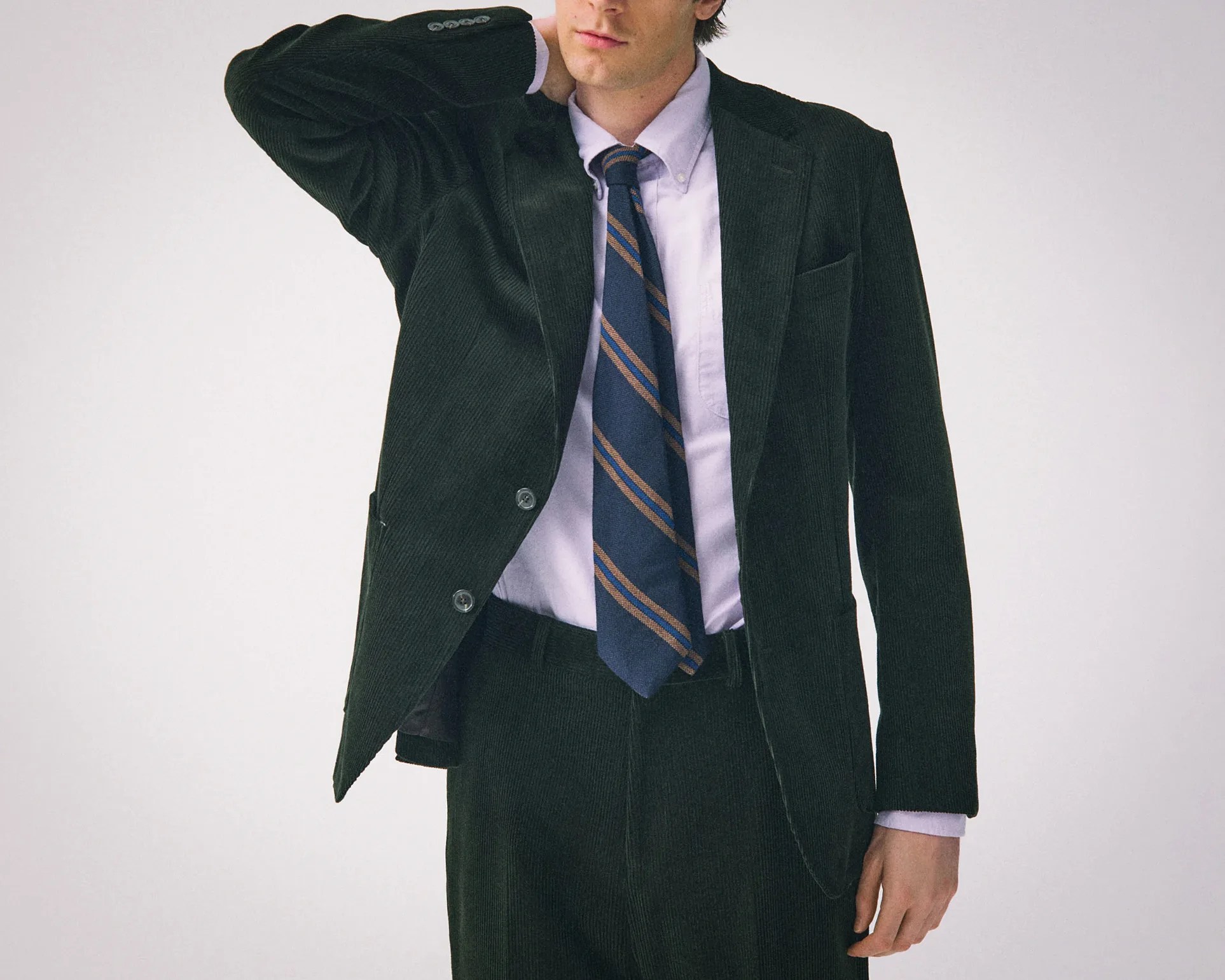 Man wearing a dark green corduroy suit with a light purple shirt and a navy blue striped tie.