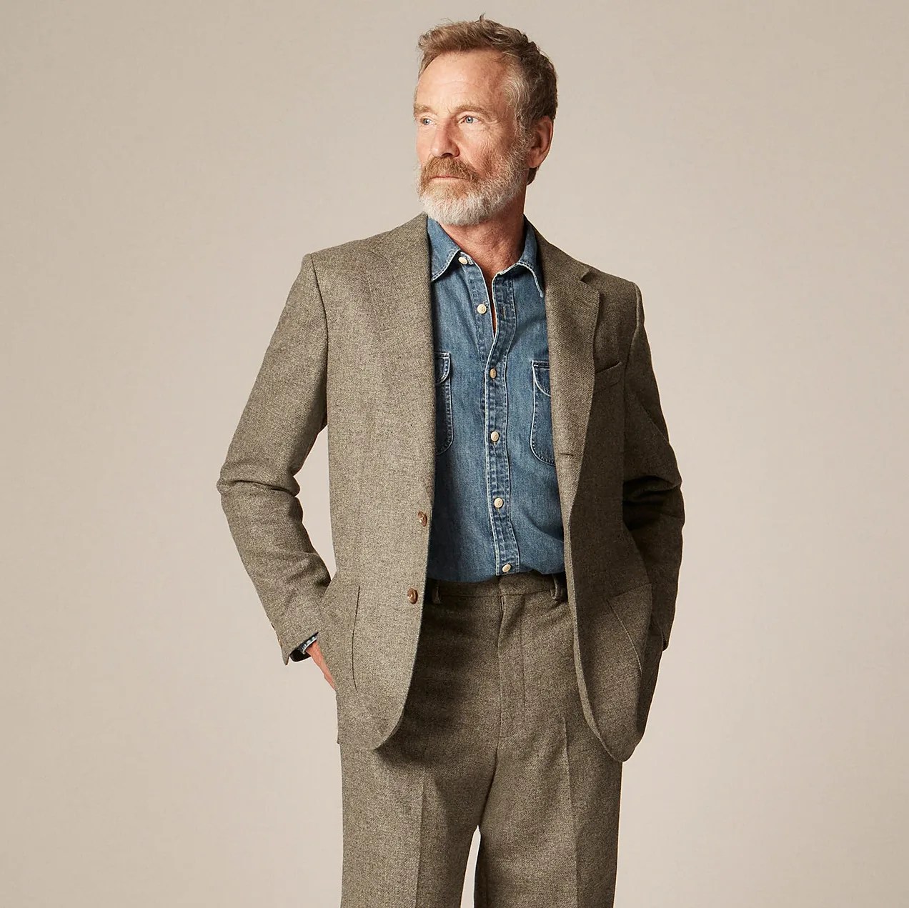 Man wearing a brown tweed suit with a blue denim button-up shirt underneath.