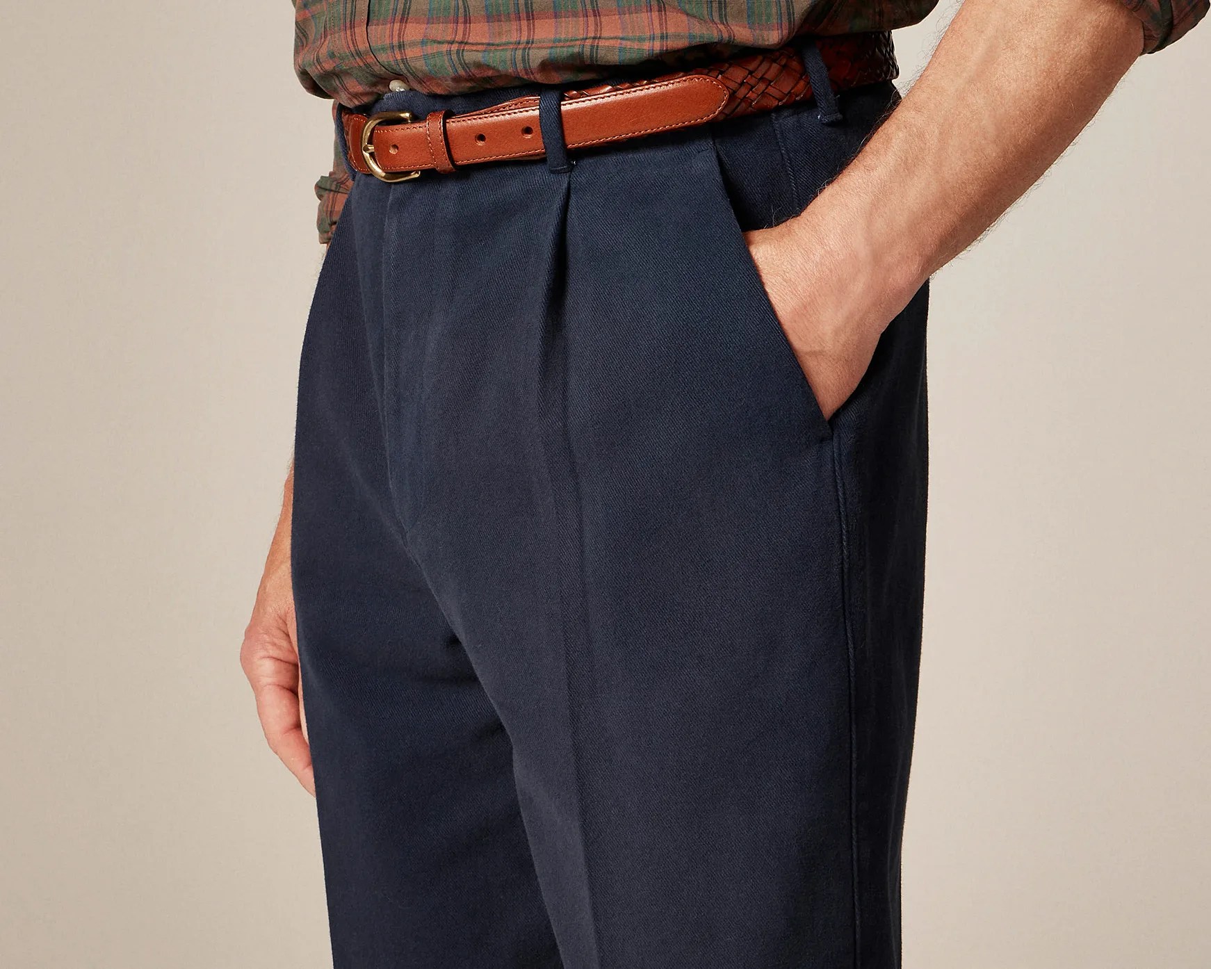 Navy blue pleated trousers with side pockets worn with a brown leather belt and plaid shirt.