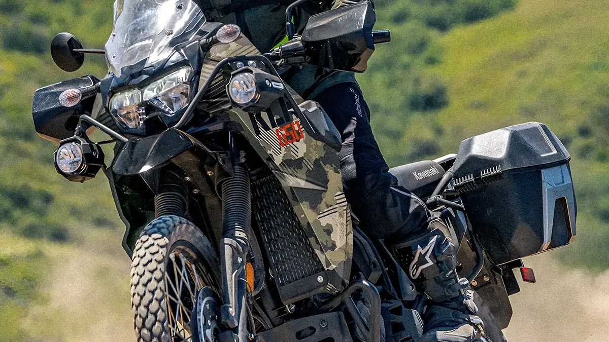 Black and camo Kawasaki KLR 650 adventure motorcycle with side panniers on a dirt trail.