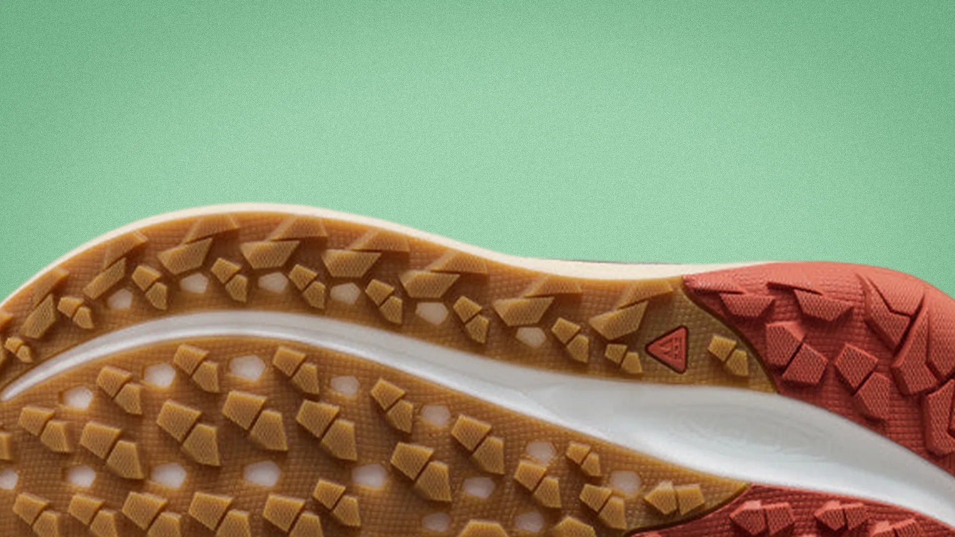 Close-up of a shoe sole with brown and red rubber treads on a green background.
