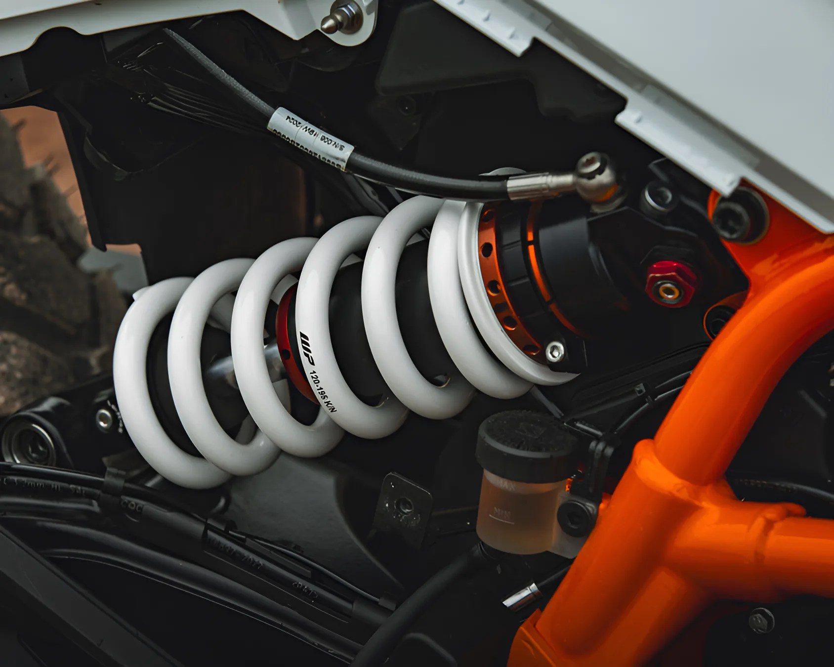 Close-up of a white coil spring suspension with black and orange components on a motorcycle frame.