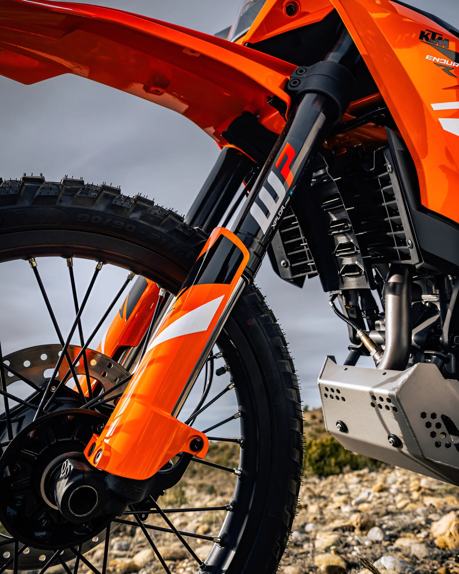 Close-up of the front suspension and wheel of an orange KTM dirt bike on rocky terrain.