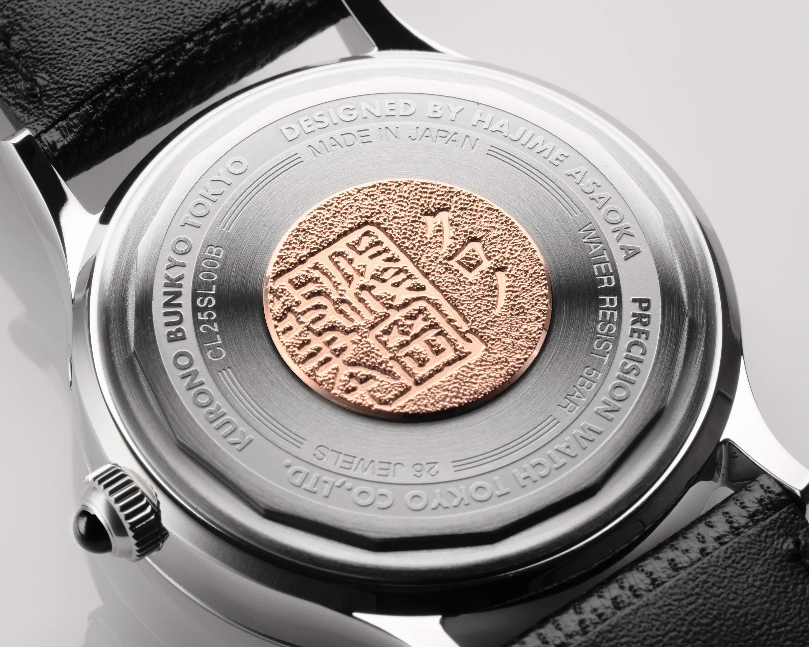 Close-up of a silver watch back with a textured rose gold medallion and engraved text around the edge.