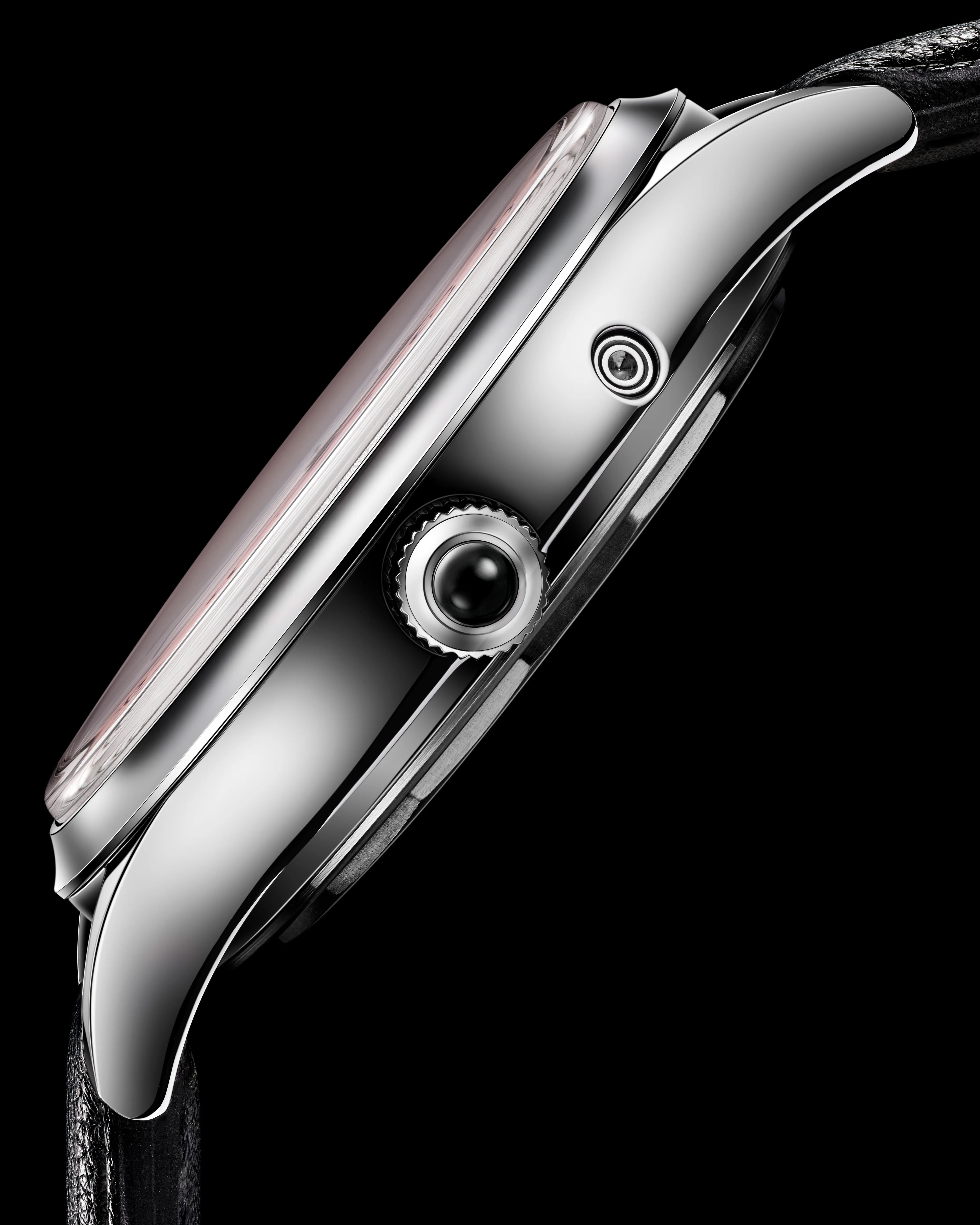 Side view of a polished silver watch case with a black crown and black leather strap against a black background.