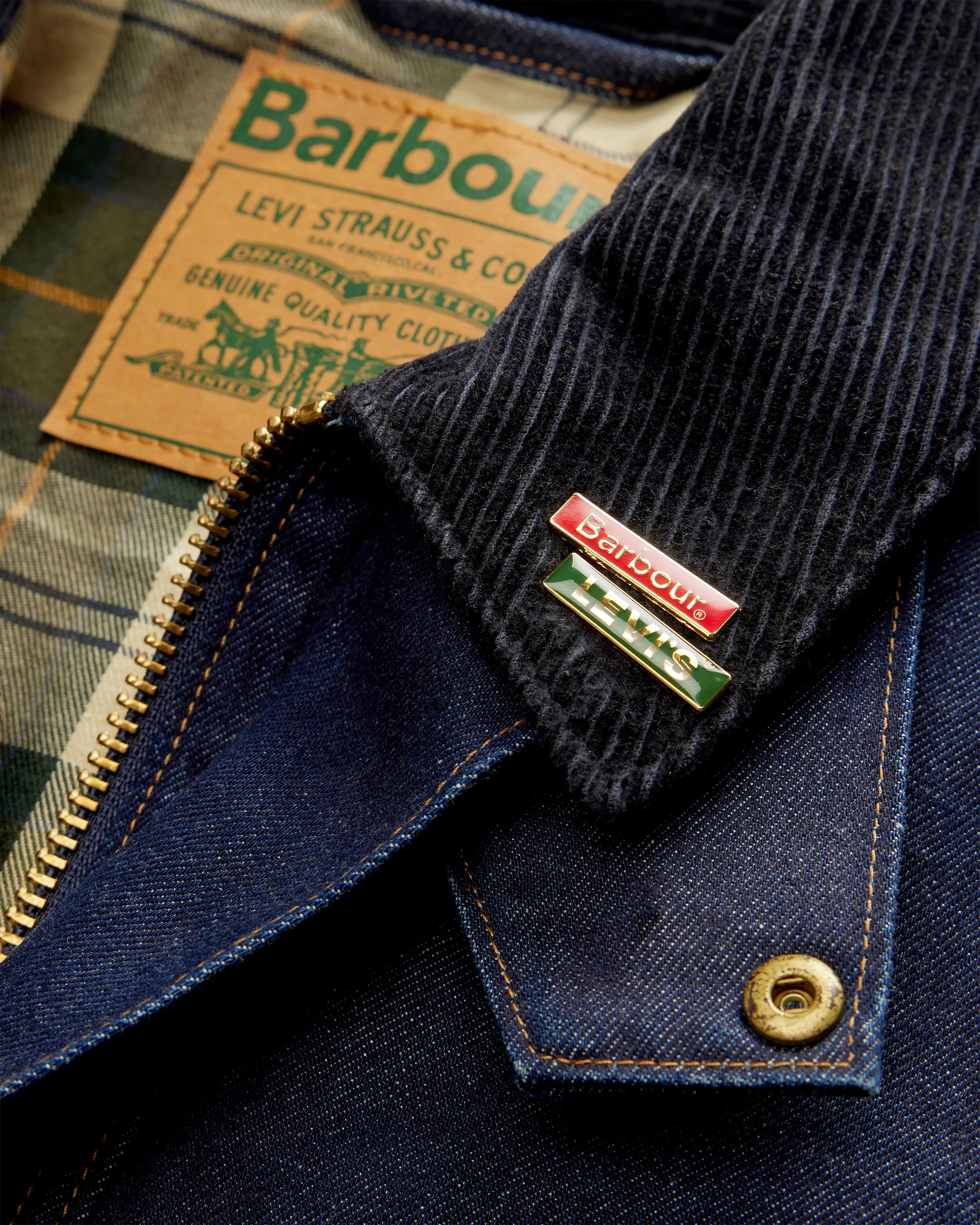 Close-up of a dark blue denim jacket with a corduroy collar featuring Barbour and Levi's enamel pins and a Barbour label inside.