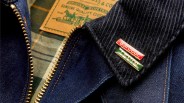 Close-up of a dark blue denim jacket with a brass zipper, black corduroy collar, and Barbour and Levi's pins attached.