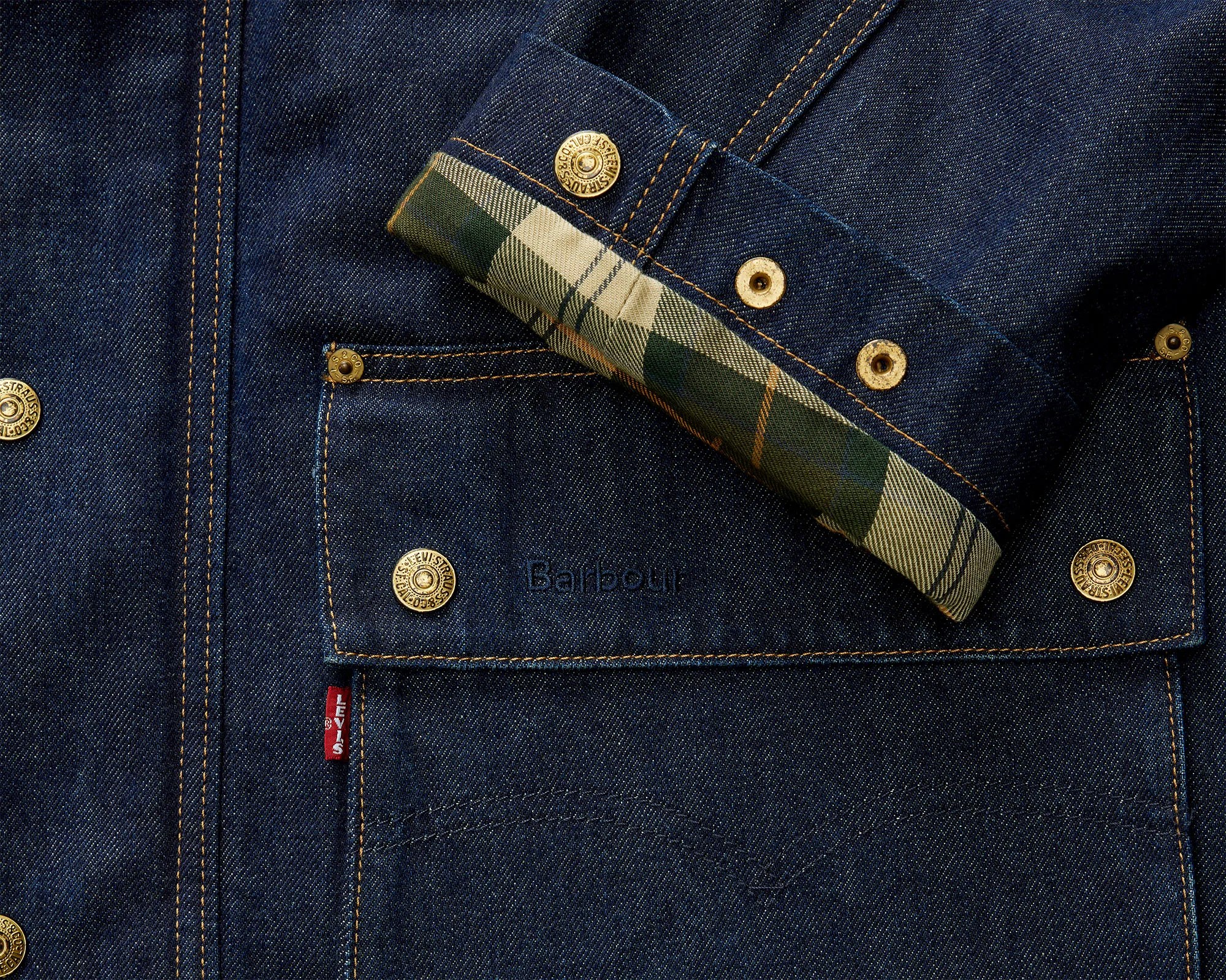 Dark blue denim jacket pocket with brass Levi's buttons and a folded cuff showing green and beige plaid lining.