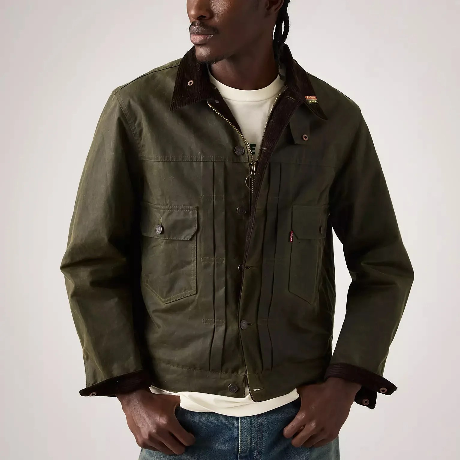 Olive green waxed cotton jacket with dark brown corduroy collar and flap pockets worn over a white shirt.