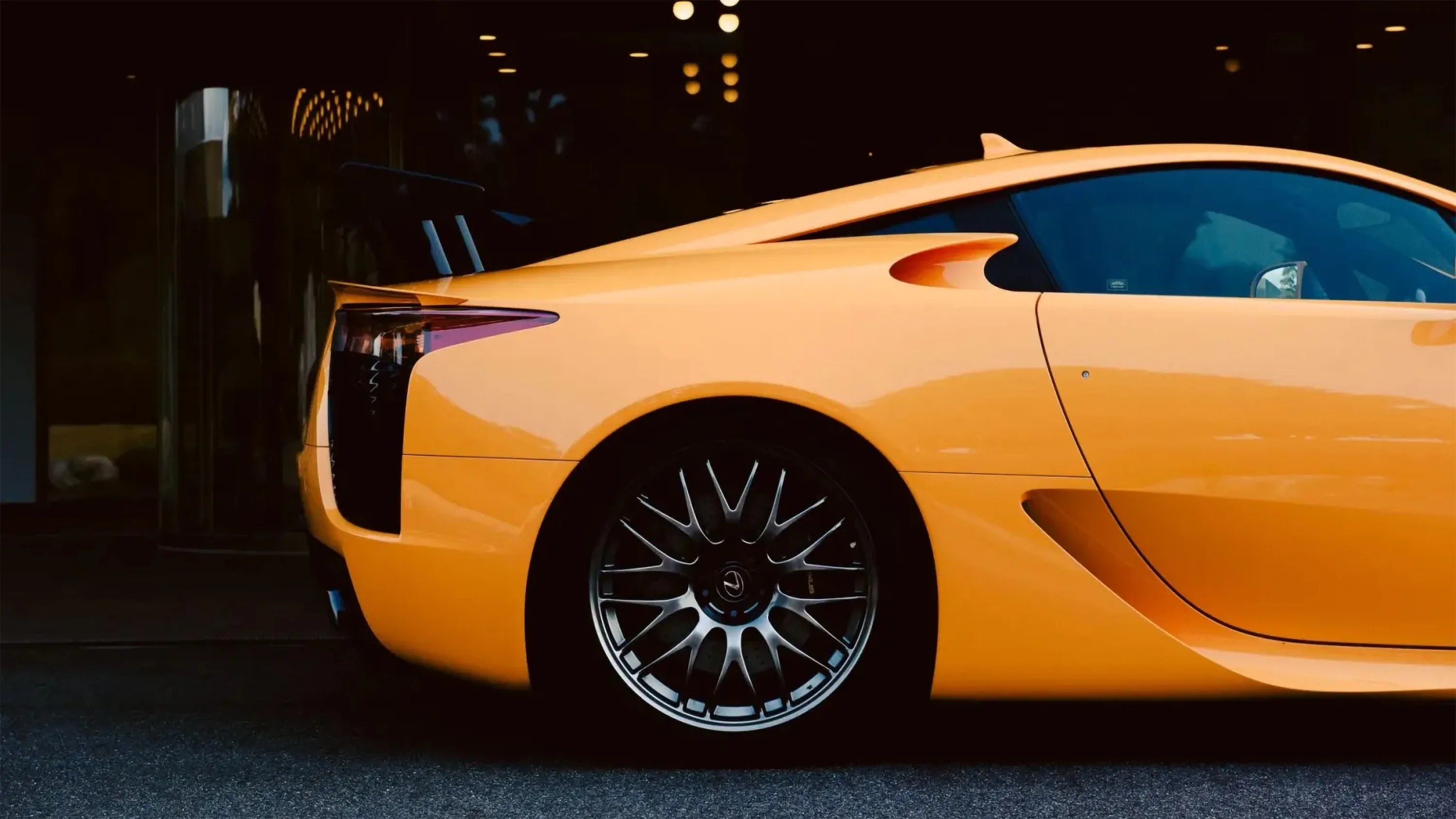 Rear side view of a yellow sports car with black multi-spoke alloy wheel and tinted windows.