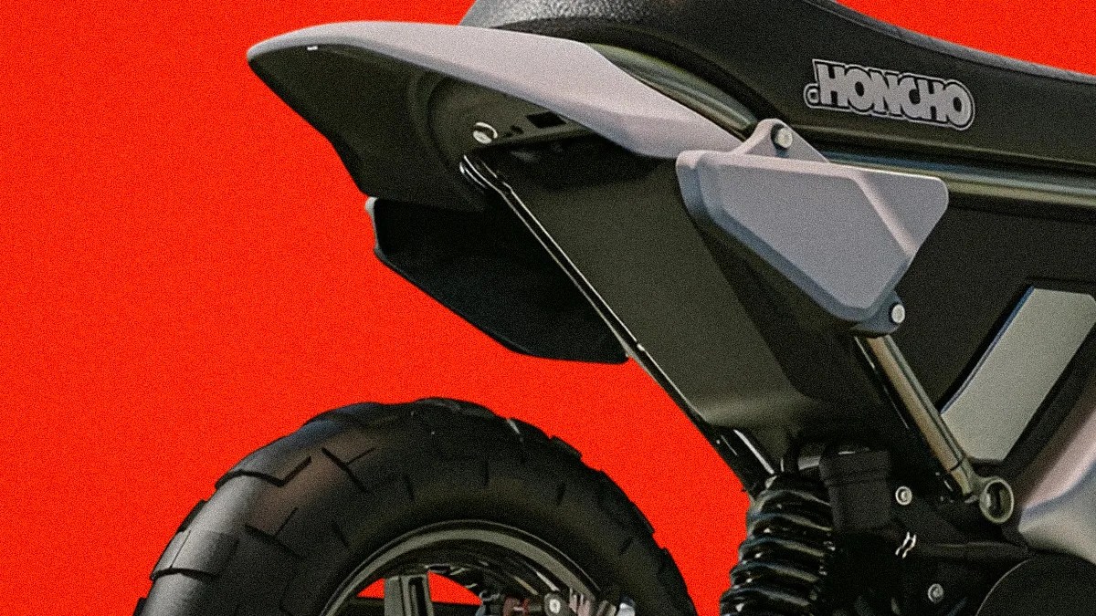 Rear section of a black and gray Honcho motorcycle with a thick tire and visible suspension against a red background.