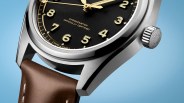 Close-up of a stainless steel watch with a black dial, gold numerals, and a brown leather strap against a blue background.