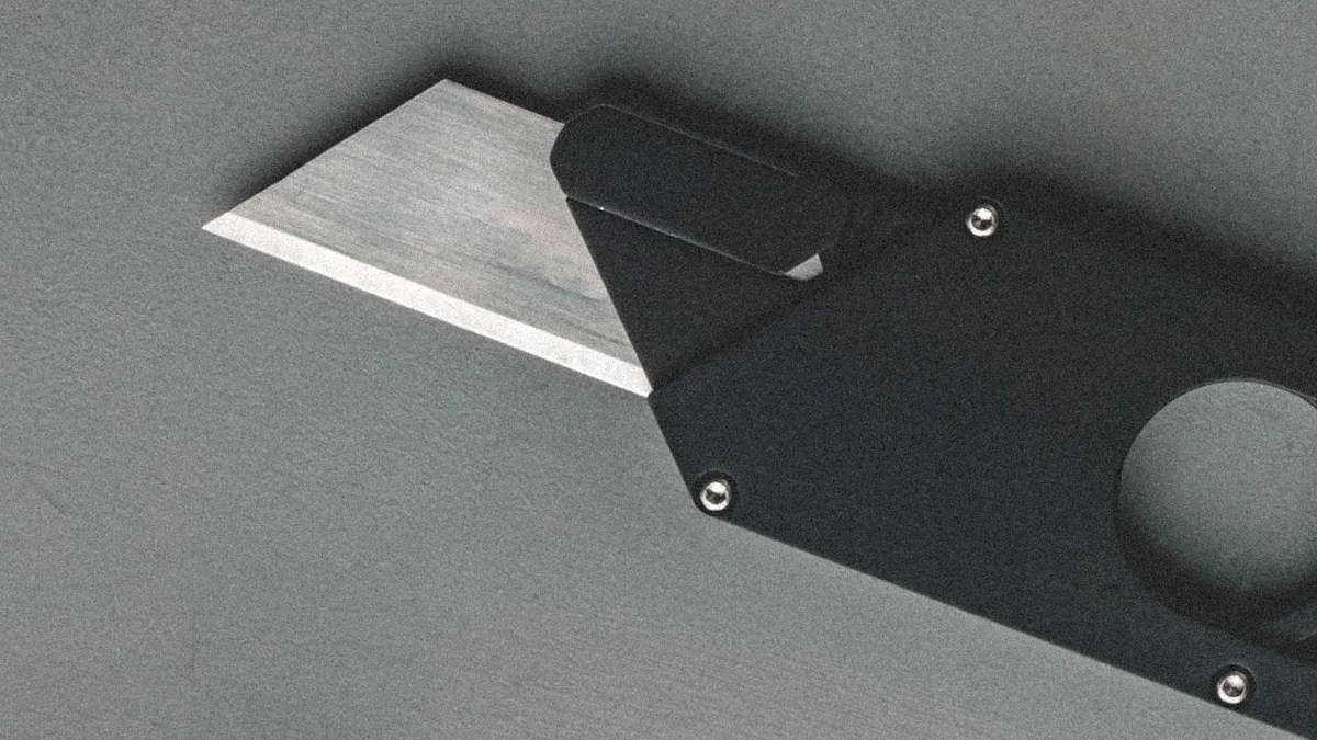 Utility knife with a partially extended silver blade and a black handle on a gray surface.