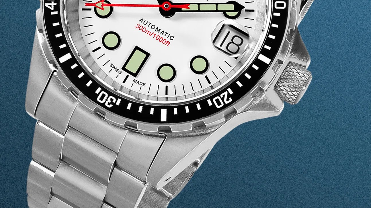 Close-up of a silver stainless steel automatic wristwatch with a white dial, black bezel, and date window showing the 18th.