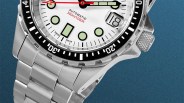 Close-up of a silver stainless steel automatic wristwatch with a white dial, black bezel, and date window showing the 18th.