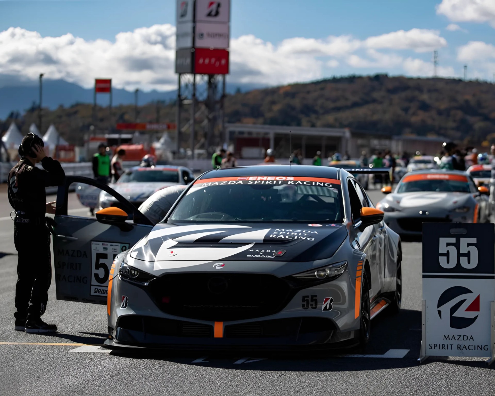 Gray and black Mazda Spirit Racing car number 55 with orange accents on a race track grid.