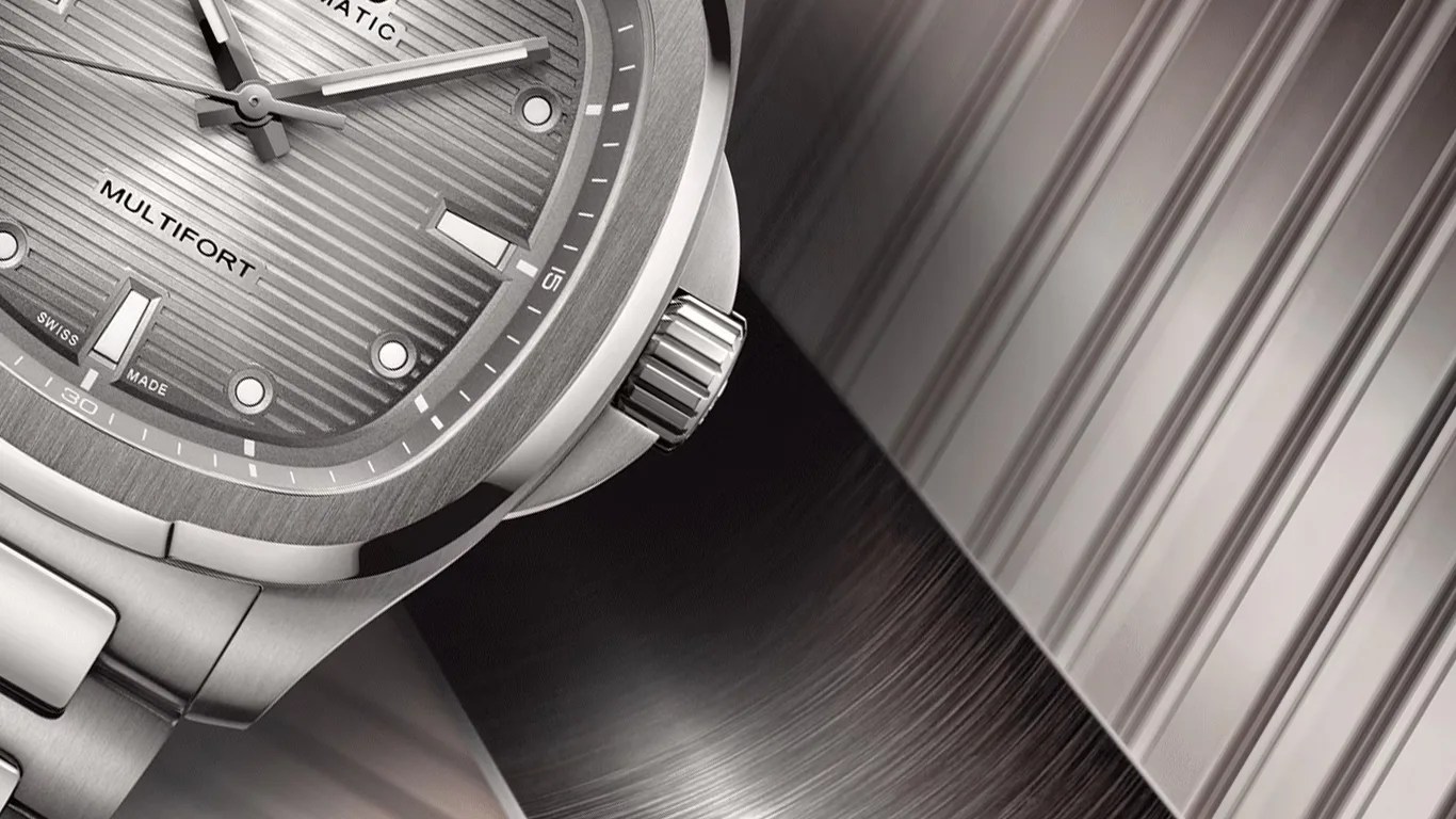 Close-up of a silver wristwatch with a textured gray dial and a ridged crown.
