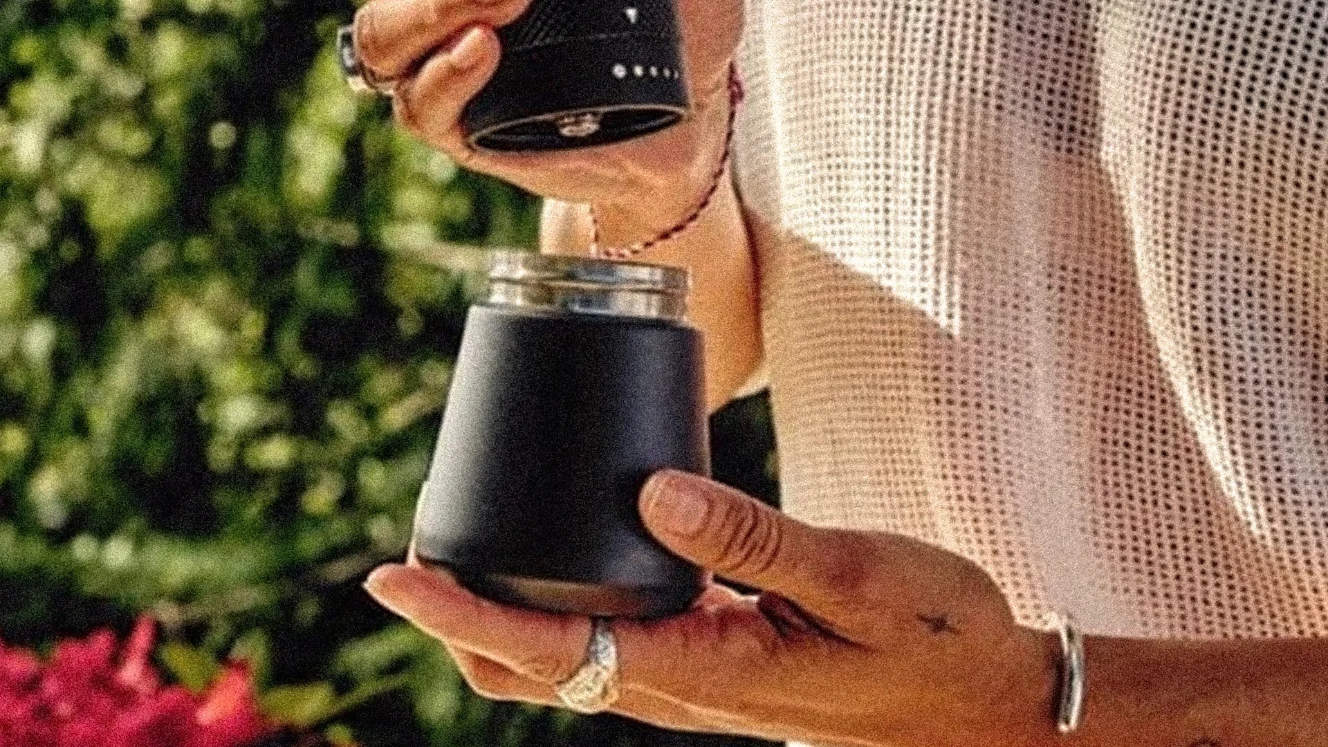 Person holding a black insulated container with a screw-on lid outdoors.