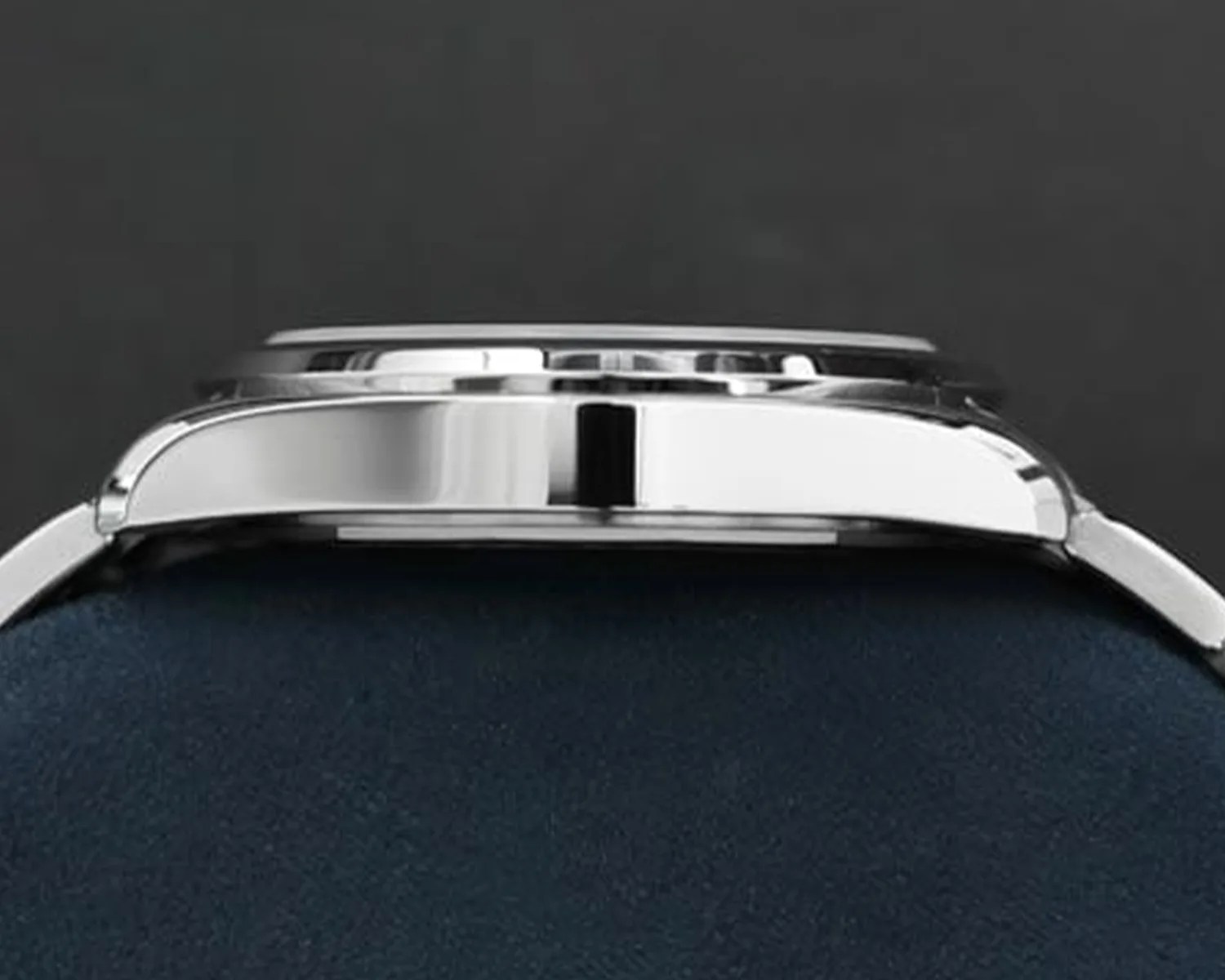 Side view of a polished silver watch case on a dark blue cushion against a dark background.