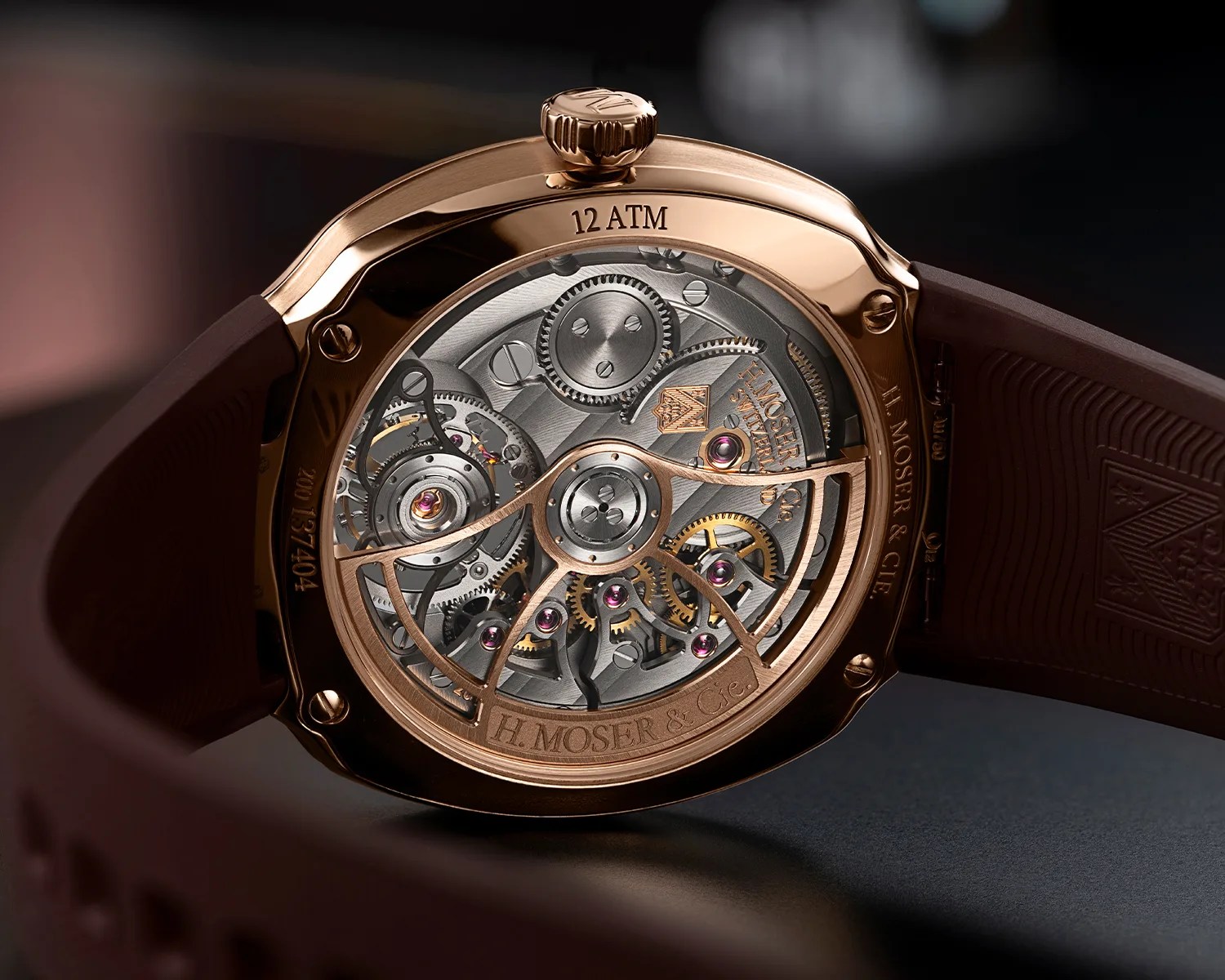 Close-up of the back of a rose gold H. Moser & Cie watch showing intricate mechanical gears and a brown rubber strap.