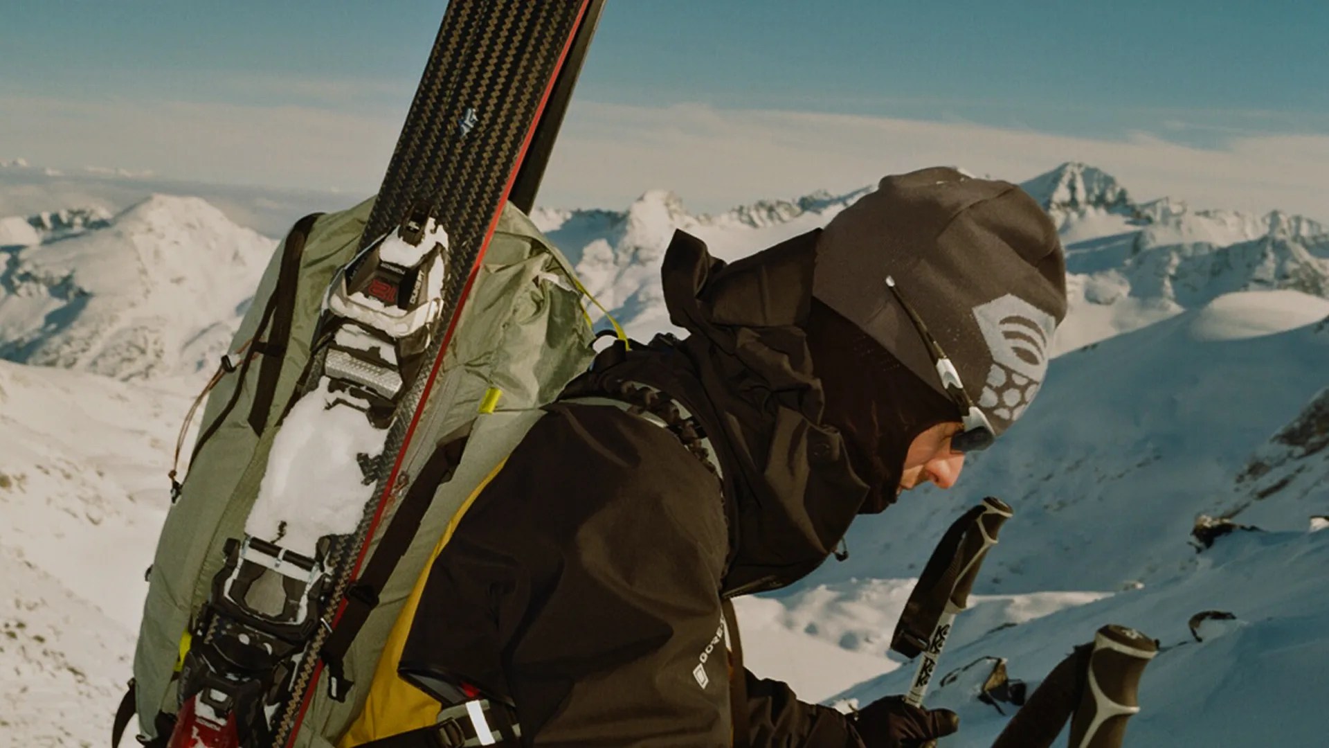 Person wearing a black jacket and gray beanie with skis and poles on a snowy mountain.