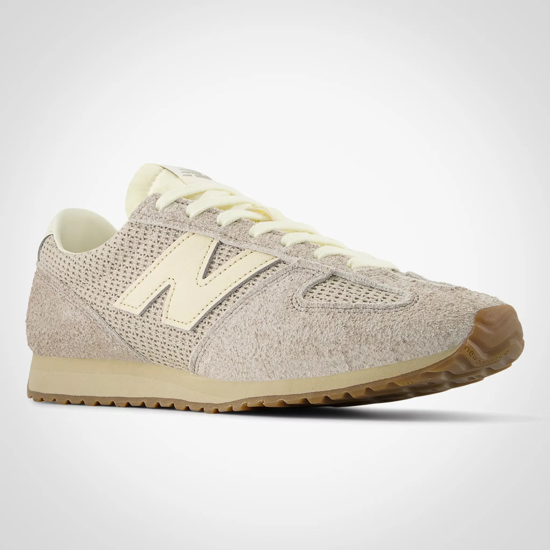 Beige New Balance sneaker with suede and mesh upper, cream laces, and gum rubber sole.