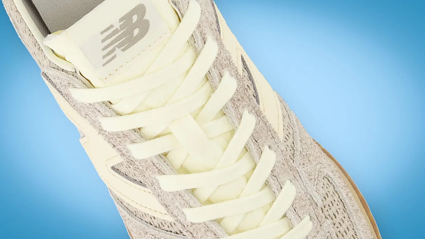Close-up of a beige New Balance sneaker with cream laces on a blue background.