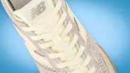 Close-up of a beige New Balance sneaker with cream laces on a blue background.