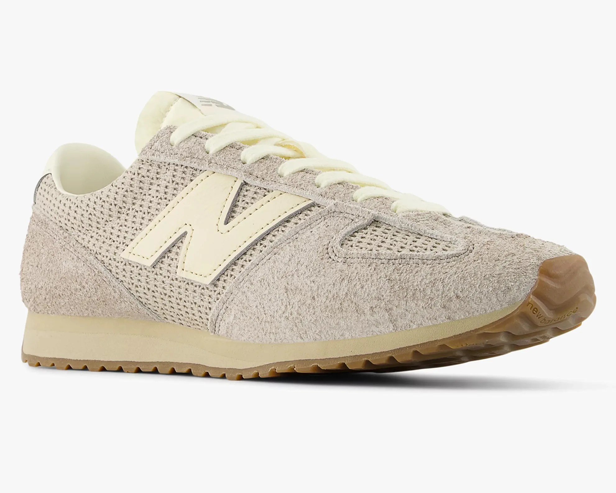 Beige New Balance sneaker with suede and mesh upper, cream laces, and gum rubber sole.