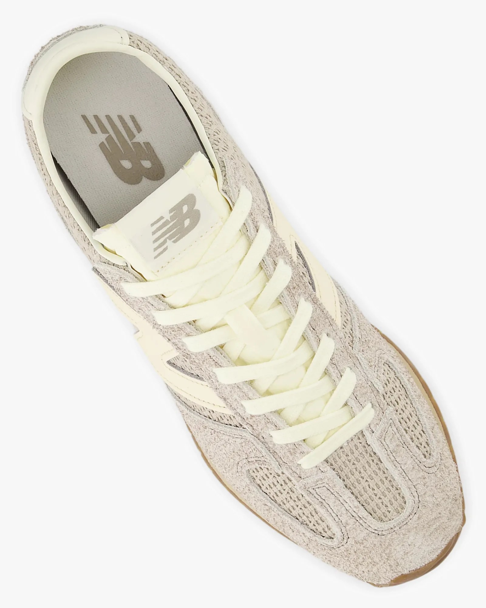 Beige and cream New Balance sneaker with suede and mesh upper, cream laces, and gum sole viewed from above.
