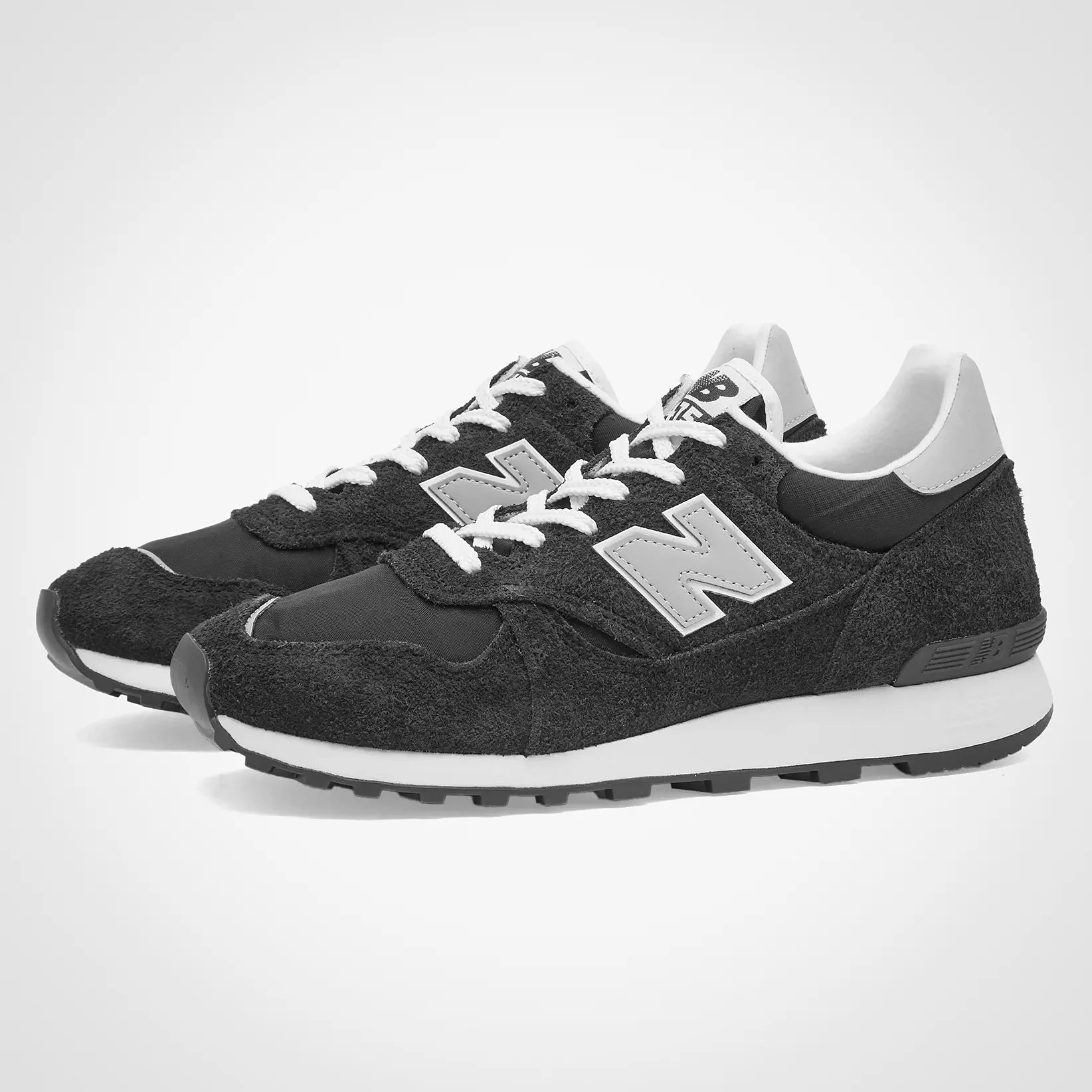 Pair of black New Balance sneakers with white laces and midsoles, featuring a suede and mesh upper.