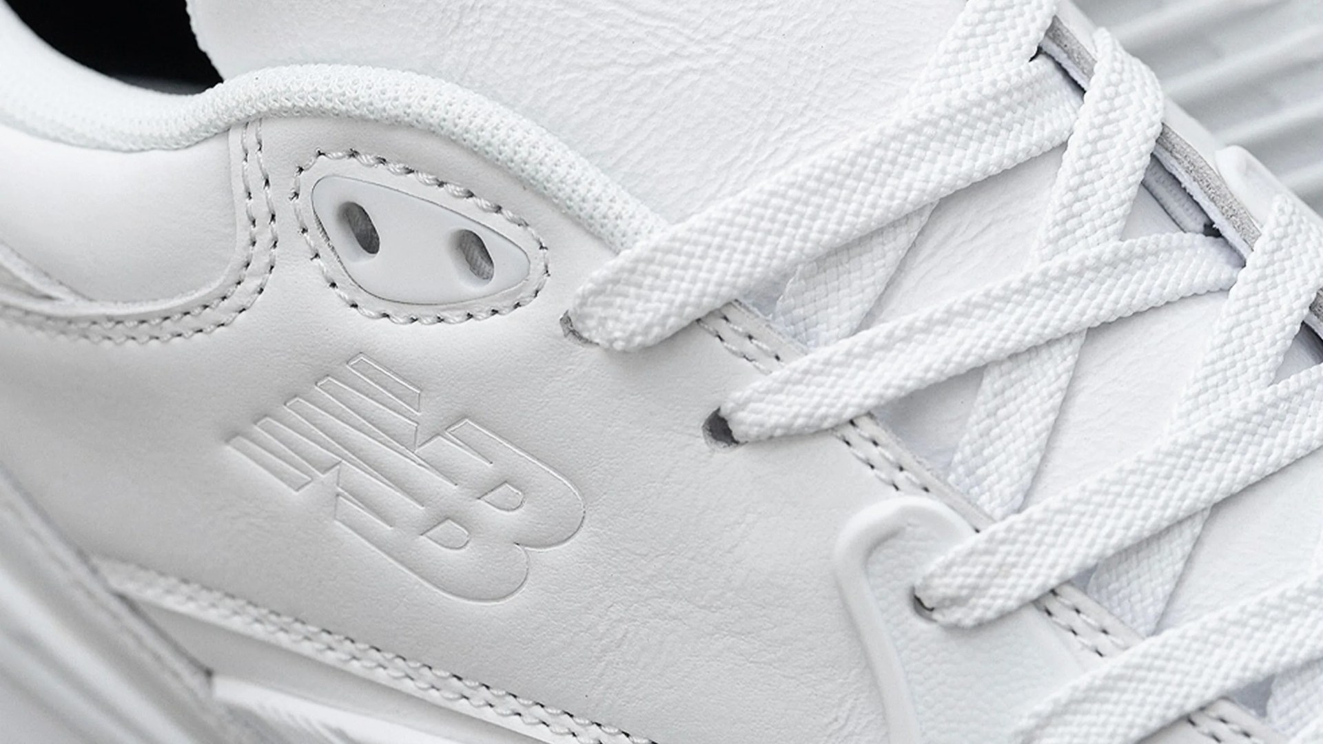 Close-up of white New Balance sneaker with embossed logo and white laces.