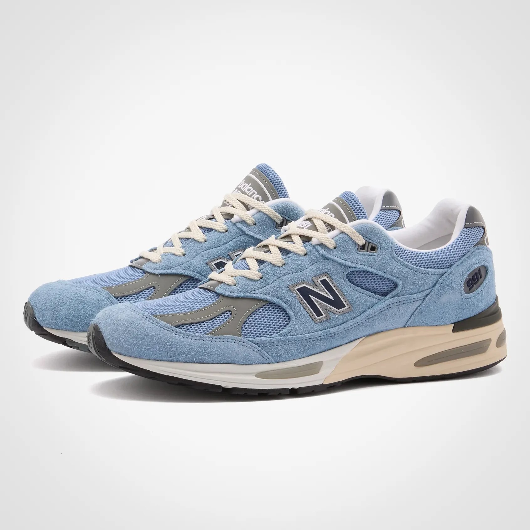 Pair of light blue New Balance 991 sneakers with beige midsoles and white laces on a white background.