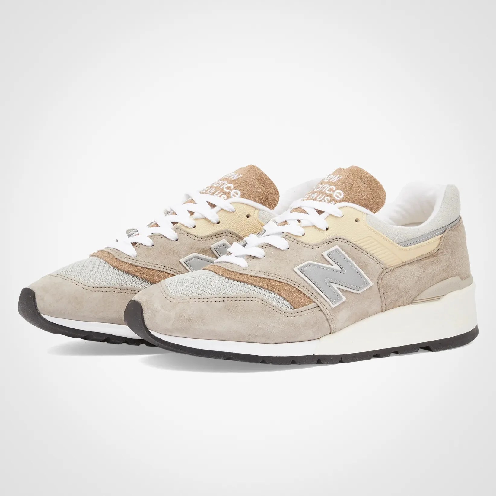Pair of beige and light gray New Balance sneakers with white laces and black soles on a white background.