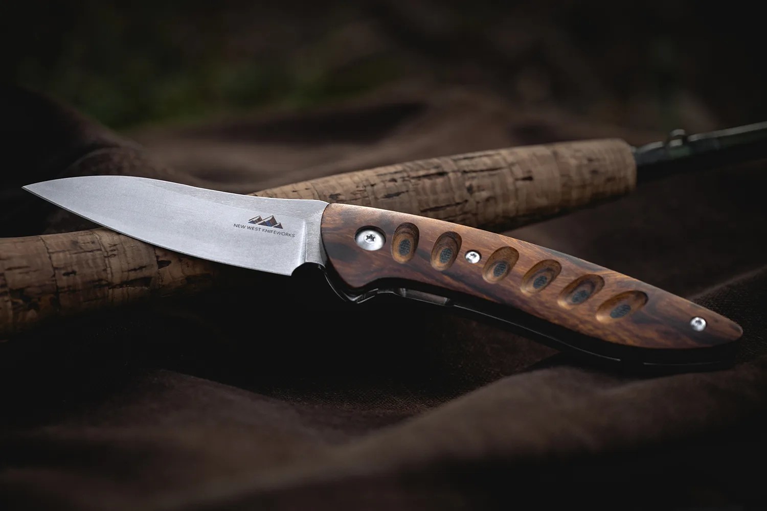 Folding knife with a stonewashed blade and a wooden handle featuring carved oval grooves.
